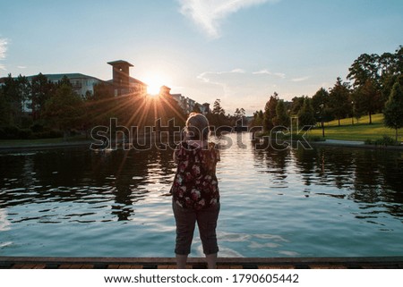 Lone woman taking a picture of the summer time sunset on the waterway in the Woodlands Texas￼