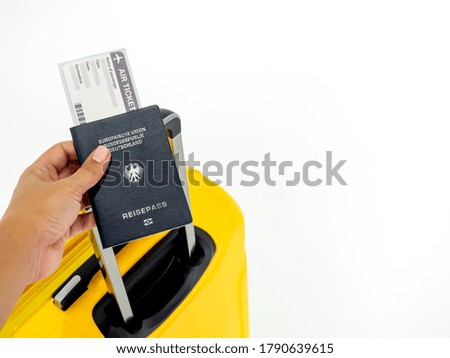 Hand holding passport and airline boarding pass ticket with yellow suitcase on white background with copy space. Blue passport of Germany and yellow luggage, travel concept.