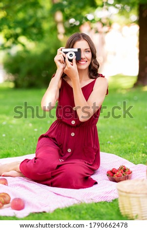 photography, leisure and people concept - happy smiling woman with camera, picnic basket sitting on blanket at summer park