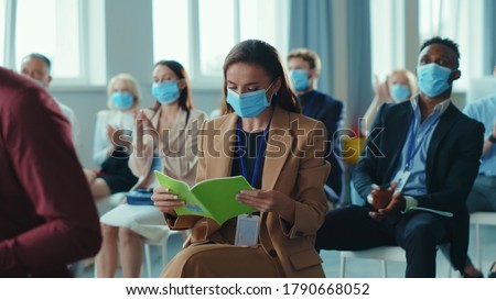 Business seminar. Quarantine. Attentive multi-ethnic corporate men and women with masks listening to business lecture presentation in conference meeting room. Social distancing. Royalty-Free Stock Photo #1790668052