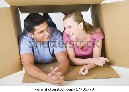 Young smiling couple lying in cardboard box and talking. Front view.