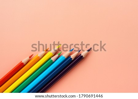 Colored pencils on pink paper, flat lay. Uneven set of rainbow pencils, copy space. Pencils lie diagonally in the lower left corner.