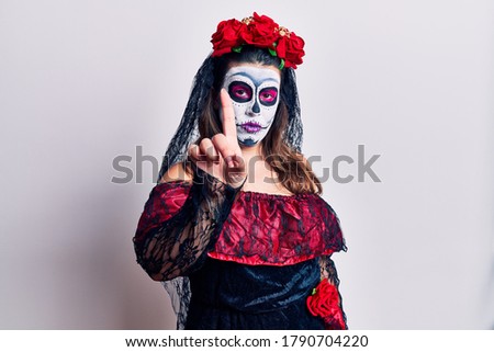 Young woman wearing day of the dead costume over white pointing with finger up and angry expression, showing no gesture 