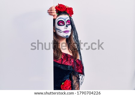 Young woman wearing day of the dead custome holding blank empty banner looking away to side with smile on face, natural expression. laughing confident. 