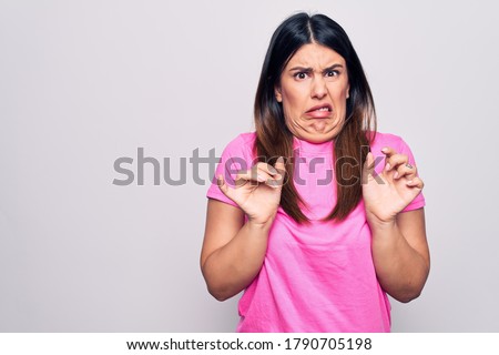 Young beautiful brunette woman wearing casual pink t-shirt standing over white background disgusted expression, displeased and fearful doing disgust face because aversion reaction. Royalty-Free Stock Photo #1790705198