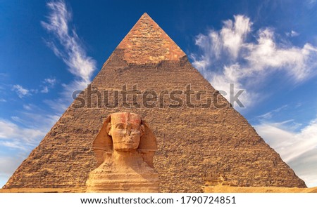 Giant statue of Great Sphinx on the background of the oldest and largest Pyramid of Giza (Pyramid of Cheops), west bank of Nile river, Cairo, Egypt; majestic atmosphere and expressive cirrus clouds Royalty-Free Stock Photo #1790724851