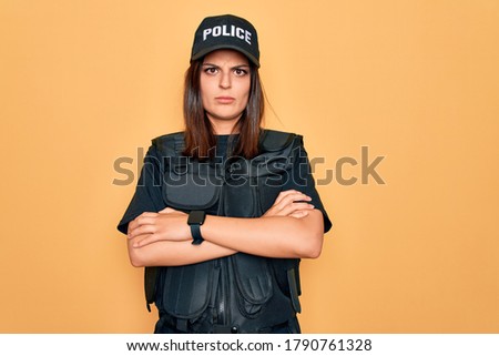 Young beautiful brunette policewoman wearing police uniform bulletproof and cap skeptic and nervous, disapproving expression on face with crossed arms. Negative person.