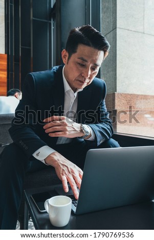 Serious business man dressed in blue suit sitting in cafeteria and using laptop stock photo