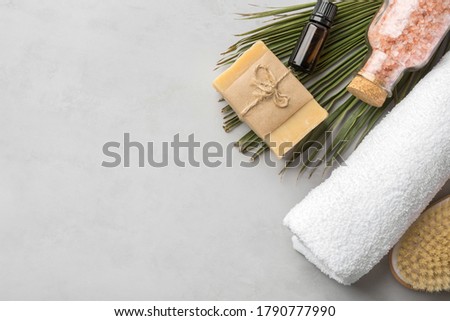 Rolled white pure cotton terry towel essential oil in amber glass bottle artisan handmade soap body brush pink Himalayan salt palm leaf on gray stone background. Spa wellness skin face care