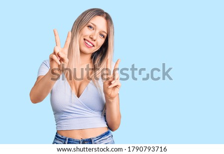 Young beautiful blonde woman wearing casual clothes smiling looking to the camera showing fingers doing victory sign. number two. 