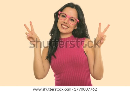 Studio shot of young happy Spanish woman smiling while giving peace sign with both hands
