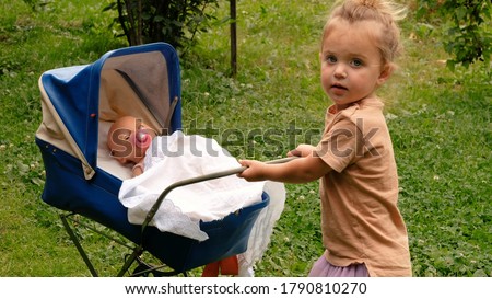 Little cute girl with ponytail playing with doll with her toy carriage on the grass