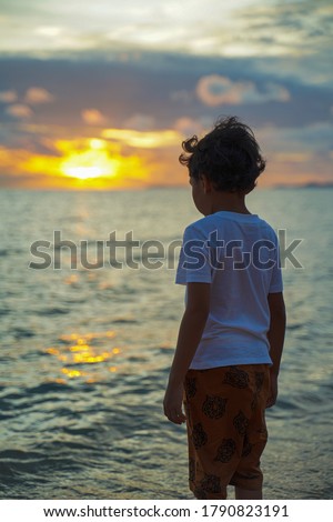 A boy standing by the beach and watching the sunset