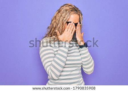 Beautiful blonde woman wearing casual striped t-shirt and glasses over purple background rubbing eyes for fatigue and headache, sleepy and tired expression. Vision problem