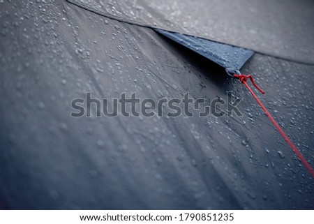 closeup detail perspective view of anchoring red rope on dark blue outdoor waterproof tent covered in rain drops