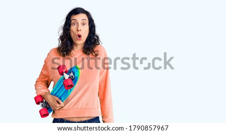 Young beautiful hispanic woman holding skate scared and amazed with open mouth for surprise, disbelief face 
