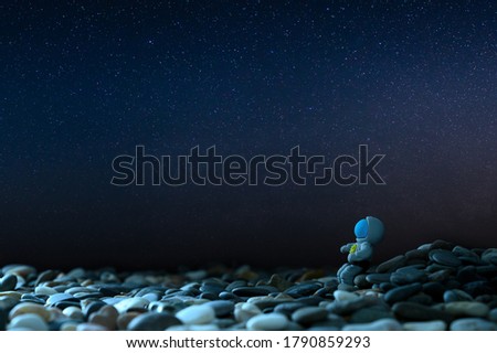 Travel to other planets concept. Feeling lonely. The figurine of the astronaut sits on the stones against the background of the starry sky. Copy space.