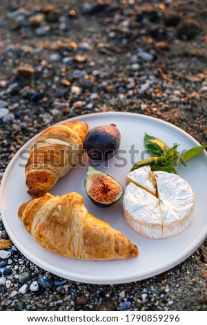 Vertical image of the beach picnic with figs, croissants and camamber cheese. Negative space.