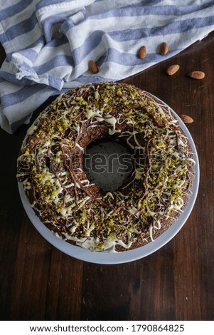 chocolate cake with pistachio and almond decorations on wooden table and striped tablecloth