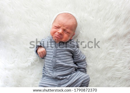 Newborn baby boy. Portrait of a little boy on white fur. Props. Close-up. In a gray striped suit
