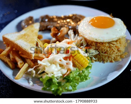 Beef steak, American fried rice, fried egg with salad, toast and french fries
