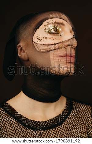 Unusual caucasian woman with pantyhose on face. Stockings advertisement or make up concept. Golden glittering on face
