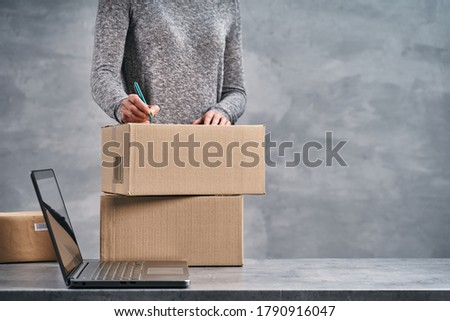 Woman writing addresses on the boxes, preparing parcels for send. Working from home