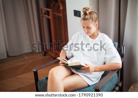 Young teen girl reading a book sitting in a chair in cozy home interier