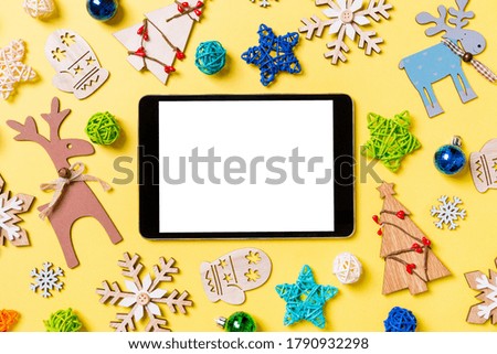 Top view of digital tablet on yellow background with New Year toys and decorations. Christmas time concept.