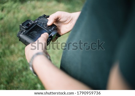 Close-up view of man hands holding camera and checking pictures. Cropped man holding professional camera and checking photos with grass in background.