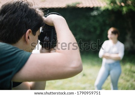 Close-up view of man photographing blurred woman outdoor. Back view of man shooting out of focus female model who is posing in front of old wall.