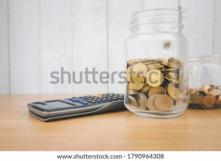 A pile of coins in a glass jar with a calculator beside Financial concepts.