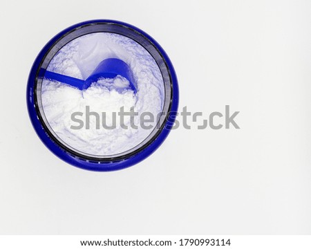 Top view of a blue container containing a white powdered sports supplement with a blue scoop Royalty-Free Stock Photo #1790993114