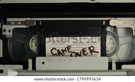 VHS video cassette recorder eject tape with old torn tag sign Game Over. Tape play video file or movie. VHS mechanics video cassette player insert tape head. Vintage concept scary movie