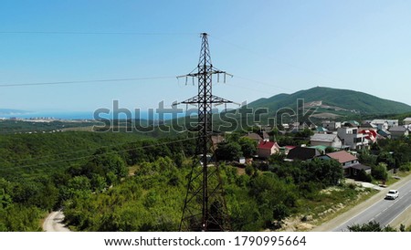 Aerial shot of an electric tower in the countryside among green mountains. The blue sky over the village is connected to electrical wires through a special device. Slow boom down.