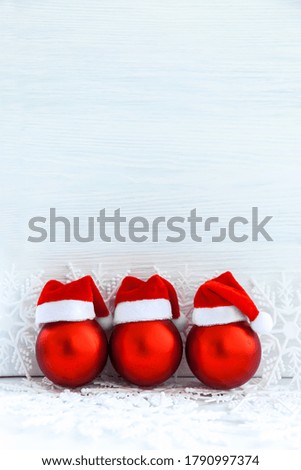 Christmas red balls with Santa hats on snow over white background. Vertical Xmas card