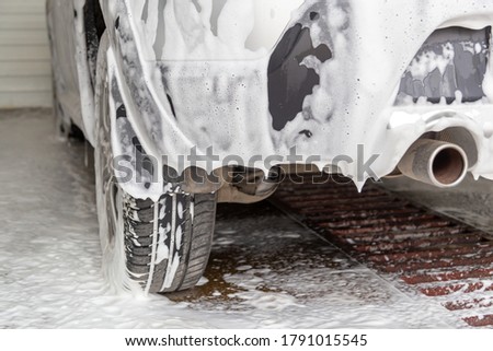 a fossil fuel car covered by soap foam while washing indoors - close-up low angle view from back with selective focus