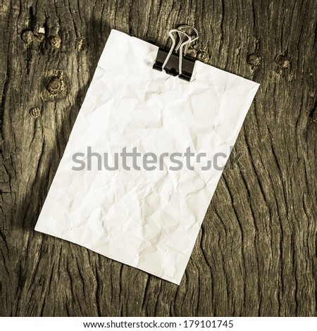 retro wrinkled paper clip on grunge wood background as blank template