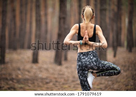Beautiful woman standing and doing yoga in forest. Exercise and meditation concept. Pay obeisance or raise hand concept. Pine wood in summer theme. Back view.