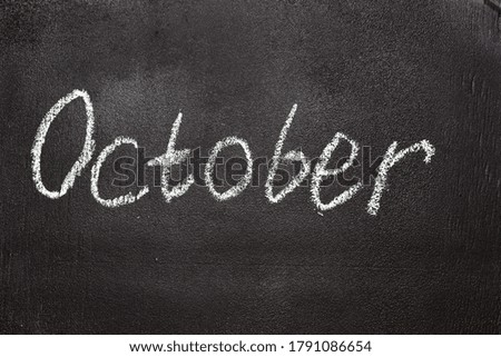 Month written in white chalk on a chalkboard. The month depicted on the chalkboard is October. Black textured school board