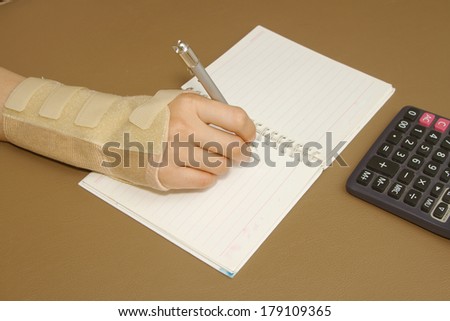 woman's hand with carpal tunnel syndrome doing calculations on sheet of paper