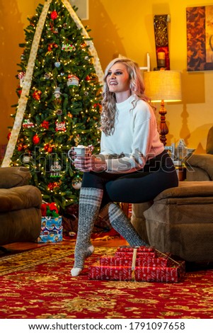 A gorgeous blonde model enjoys the holiday season at home with a Christmas tree and presents