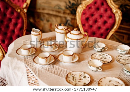Close-up of tea sets on a white lace tablecloth with plush red chairs.