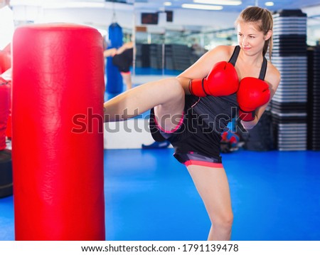 Glad cheerful  smiling woman boxer is training kick in box gym.
