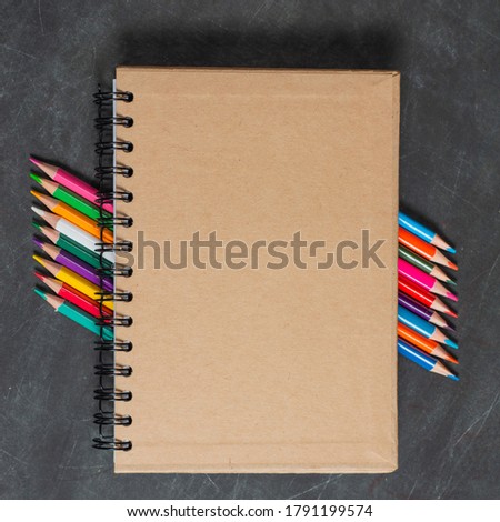 brown notebook lies on a set of multi-colored pencils on a dark background