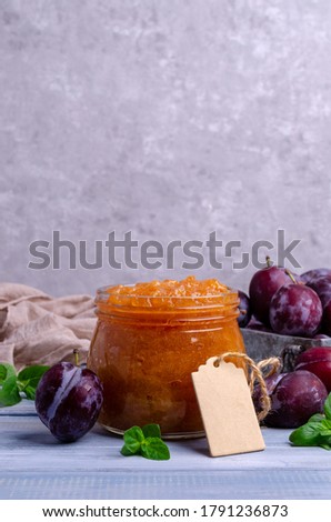Yellow plum jam in a glass jar on a blue wooden background with fresh fruit. Selective focus.