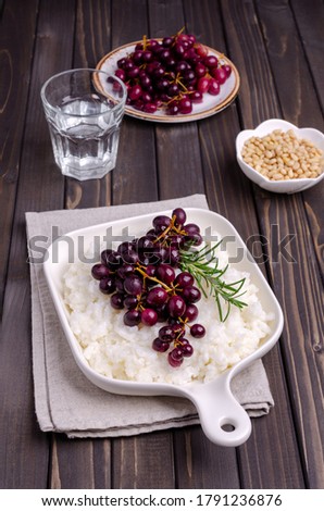 Boiled white rice with stewed grapes and rosemary in a ceramic dish on a wooden background. Selective focus.
