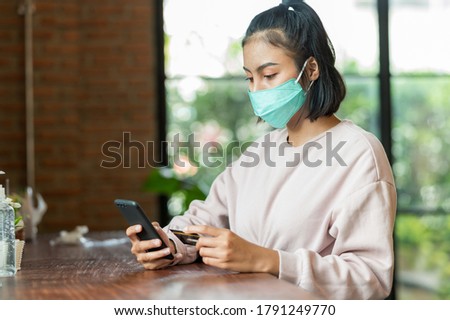 Woman wearing surgical mask in cafe shopping online with Mobile Phone