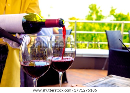 The waiter in the restaurant on the terrace pours red wine into glasses