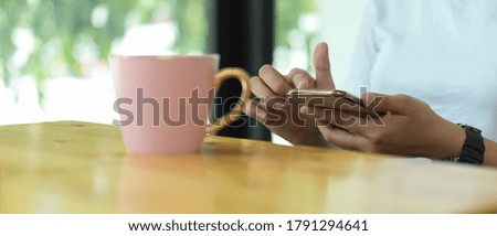Close up view of male hands using smartphone while siting at coffee table in coffee shop
